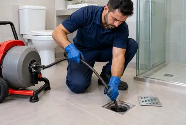 Técnico trabalhando no desentupimento de ralo, com ferramentas em uso.